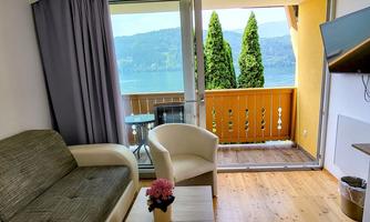 A cozy living room with a sofa and a view of the lake. The balcony with plants offers a beautiful view of the surrounding nature.