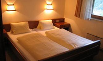 A cozy room with a double bed and soft lighting. The windows let in daylight and create an inviting atmosphere.