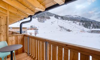 A balcony with a view of snow-covered mountains and a ski slope. The wooden paneling and the table give the room a cozy atmosphere.