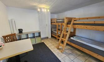 A simple room with wooden bunk beds. There is a table, a chair, and access to the door.