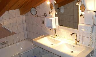 A modern bathroom with two sinks and a large mirror. There is a bathtub and wooden ceilings that create a cozy atmosphere.