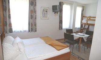 A simple room with a double bed and a bunk bed. There are four chairs at the table and a window provides plenty of natural light.