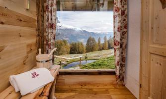 A cozy wooden cabin with a view of the mountains and a green landscape. Daylight is streaming through the window, creating an inviting atmosphere.