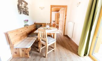 A cozy dining area with light wood and a small table set. Plants and an inviting atmosphere contribute to a pleasant environment.