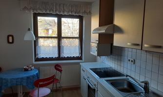 A bright kitchen with a window that lets in a lot of light. The room is simply furnished with a blue table and red chairs.