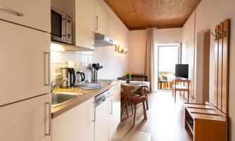A modern kitchen with white cabinets and a small seating area. The room is bright and inviting, with plenty of natural light.