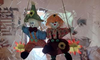 Two cheerful fabric clowns are sitting on a swing. They are wearing colorful clothes and have sunflowers as decoration.
