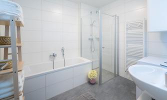 A modern bathroom with a bathtub and shower. There are bright tiles and a practical shelf for towels.