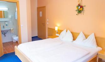 A cozy hotel room with a double bed and bright walls. A bathroom is visible in the background.