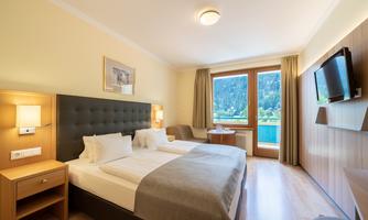 A cozy hotel room with two single beds and a beautiful view of the mountains. The decor is modern and bright with a television and a sitting area.