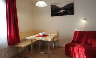 A cozy dining area with a wooden table and red curtains. A painting of a mountain landscape hangs on the wall.