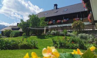 An idyllic country house with blooming plants and a green garden. The sky is blue with some clouds.