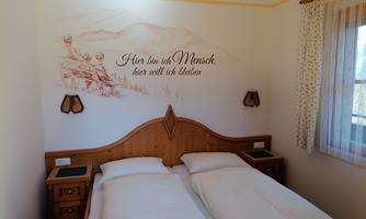A cozy bedroom with two single beds and wooden furniture. On the wall, there is a decorative quote and a simple, bright design.
