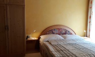 A cozy bedroom with a large bed and a wooden dresser. The walls are painted in a warm shade of yellow, and there are two bedside lamps.