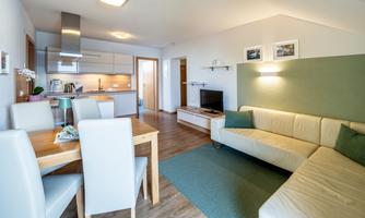 A modern apartment with an open living and dining area. The decor is bright and friendly, featuring a kitchen and a cozy sofa.