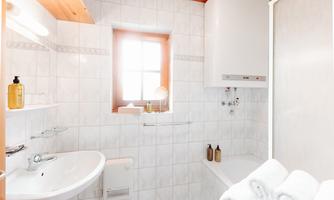 A modern bathroom with bright tiles and a window. On the sink, there are care products, and fresh towels are ready.