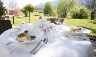 An elegant outdoor table with two beautiful plates showcasing delicious meals. In the background, a wonderful view of the Karawanken.