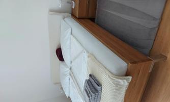 A tidy bedroom with a wooden bed and fresh bedding. Next to the bed is a nightstand with a lamp.