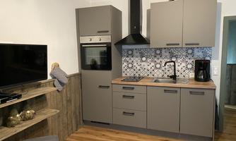 A modern kitchen with gray cabinets and a wooden work table. In the background, a decorative tiled splashback can be seen.