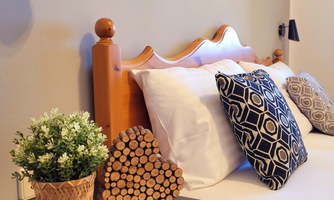 A cozy bedroom with a wooden headboard and two pillows. On the nightstand, there is a small flower pot and a heart-shaped decoration made of wooden logs.