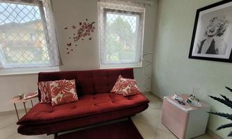 A cozy room with a red sofa and decorative cushions. Pictures hang on the walls, and there is plenty of natural light from the windows.