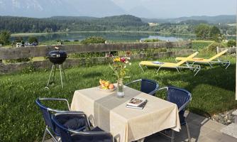 A beautiful outdoor area with a table, chairs, and a barbecue spot. In the background, the lake and the mountains can be seen.