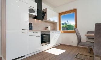 A modern kitchen with white cabinets and a window that overlooks a green landscape. The space is bright and invitingly designed.