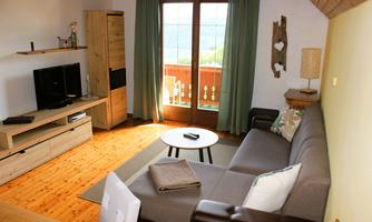 A cozy living room with a gray sofa and a small table. Large windows offer a view of the outdoor landscape.
