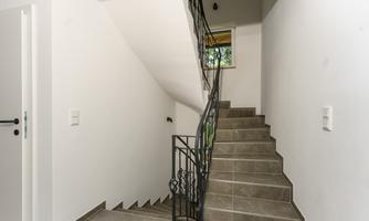 A modern staircase in a bright hallway. The room is simple and well-lit, with a window on the upper level.