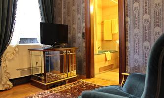 An elegant room with a television and a comfortable chair. In the background, a bathroom with yellow towels is visible.