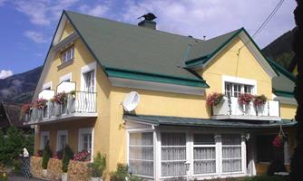 A charming yellow house with green roofs and blooming balconies. The surroundings are characterized by mountains and a peaceful atmosphere.