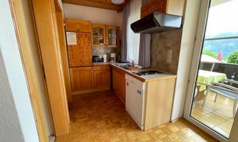 A modern kitchen with wooden cabinets and space for a dining area. Large windows provide plenty of natural light.