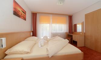 A cozy bedroom with a double bed and two pillows. Large windows let in plenty of daylight and offer a view of the outdoor routine.