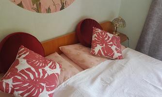 A cozy bedroom with a bed and decorative pillows in red and white colors. Next to the bed stands a table lamp in an elegant design.