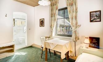 A simple room with a table and chairs. The windows are decorated with curtains and there is a small bathroom in the background.