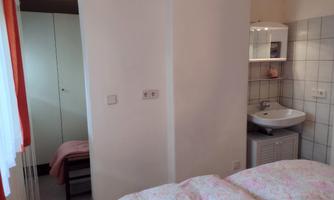 A simple bedroom with two beds and a sink. In the background, there is a small wardrobe and an adjacent bathroom.