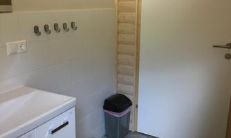 A small bathroom with a sink and a trash can. There are hooks on the wall for hanging towels or clothes.