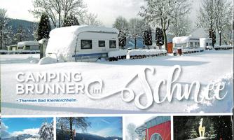 A snowy campsite with RVs under snow-covered trees. The sky is clear and the landscape looks peaceful.