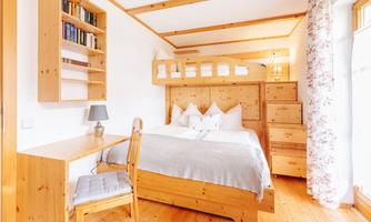 A cozy bedroom with wooden furniture and a double bed. There is also a desk and a shelf with books.