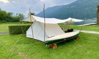 A tent stands on a green meadow, surrounded by mountains. Next to the tent is a canoe, ready for adventure.