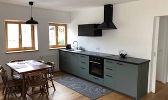 A modern kitchen with gray cabinets and a stove. Wooden chairs are at the table and there is plenty of natural light through the windows.