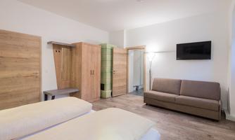 A bright room with two beds, a couch, and a television on the wall. The furniture is made of wood and creates a cozy atmosphere.