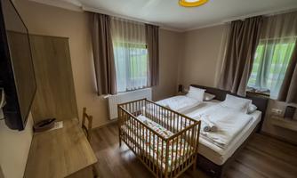 A cozy bedroom with two beds and a crib. The rooms are bright and modernly furnished, with large windows and a television.