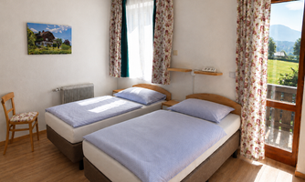 A cozy room with two single beds and a beautiful view of the mountains. The large windows let in plenty of light and the floral curtains give the room a warm atmosphere.