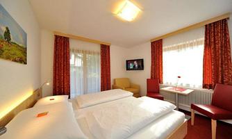 A cozy hotel room with two single beds and red curtains. There is a small table and a television on the wall.