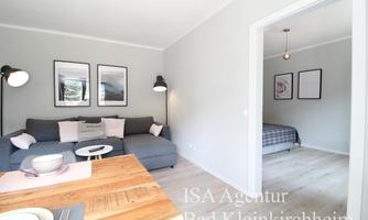 A modern apartment with a cozy living room and a dining area. In the background, there is a bedroom with a bed.