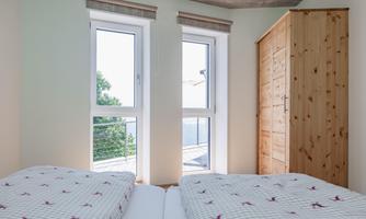 A cozy bedroom with two beds and large windows. A bright wooden dresser complements the modern decor.