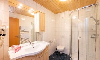 A modern bathroom with a shower and a sink. The walls are brightly tiled and the ceiling is made of wood.