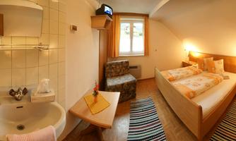 A cozy hotel room with a double bed and a small seating area. The room has a private bathroom and plenty of natural light.