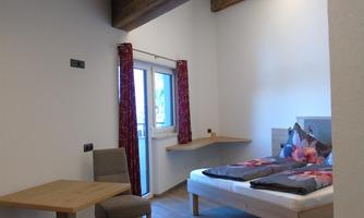 A modern room with a double bed and a small dining area. Large windows provide plenty of daylight.